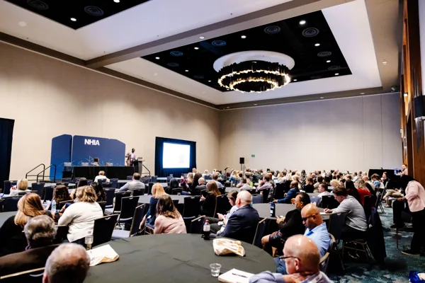 Wide view of a packed preconference classroom with attendees at rounds facing the screen.