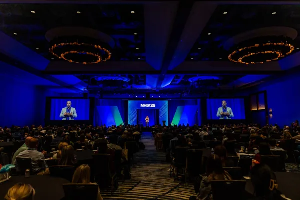 Wide view of the general session ballroom with blue stage lighting and a large audience.