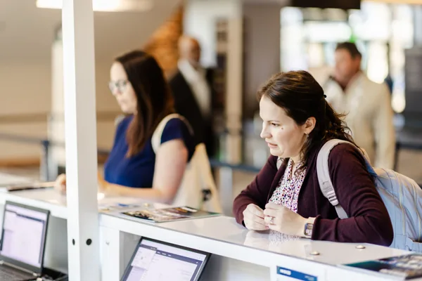 Two attendees work at laptops at a conference help counter.