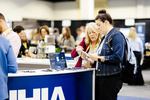 Attendees gather at the NHIA counter with laptops open.