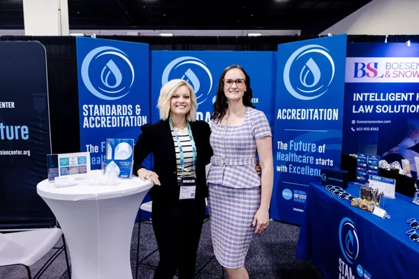 Two attendees stand at a high-top table in front of an exhibit booth.