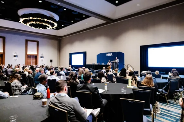 A speaker presents to a full preconference session room with a projection screen at the front.