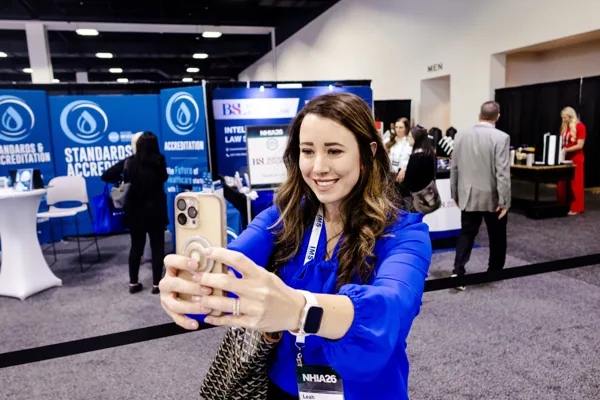A conference attendee films with her phone in front of an exhibit booth.