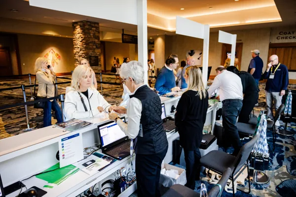 Staff help attendees at a registration counter lined with monitors.