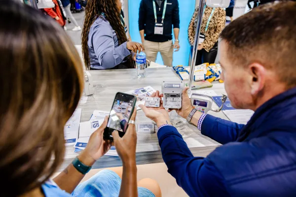 An attendee holds up a phone, its screen visible, at a conference table.