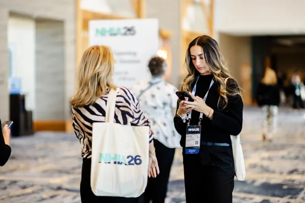 An attendee carries an NHIA26 canvas tote bag over her shoulder.