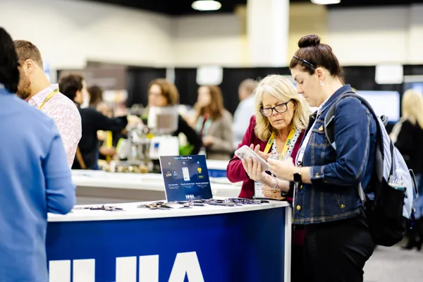 Attendees use screens and laptops at the NHIA counter on the expo floor.