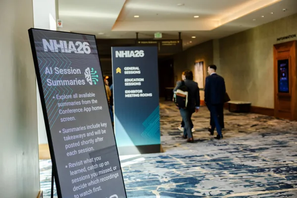 Branded NHIA26 session signage lines the education-level concourse as attendees pass.