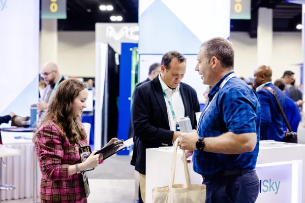 An attendee reads a printed handout while talking with exhibitors on the expo floor.